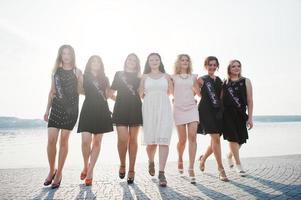 Gruppe von 7 Mädchen in Schwarz und 2 Bräute beim Junggesellinnenabschied am sonnigen Strand. foto