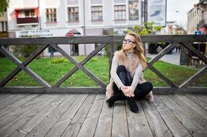 Blondes Mädchen im Pelzmantel sitzt auf Holzboden im Freien. foto