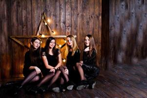 vier süße freundinnen tragen schwarze kleider gegen große leichte weihnachtssterndekoration auf hölzernem hintergrund. foto