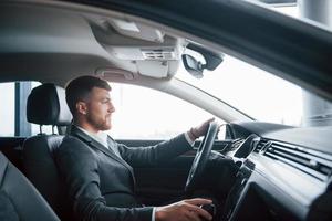 aufrichtiges Lächeln. moderner geschäftsmann, der sein neues auto im autosalon probiert foto