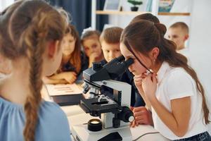 Mädchen, das Mikroskop untersucht. gruppe von kinderschülern im unterricht in der schule mit lehrer foto