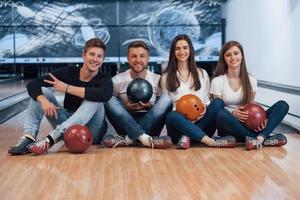 auf dem Boden sitzen. Junge, fröhliche Freunde haben an ihren Wochenenden Spaß im Bowlingclub foto