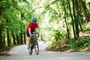 Foto in Bewegung. Radfahrer auf dem Fahrrad ist an sonnigen Tagen auf der Asphaltstraße im Wald