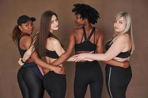 Blick hinter die Kamera. Gruppe multiethnischer Frauen, die im Studio vor braunem Hintergrund stehen foto