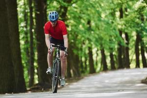 Freizeitaktivitäten. Radfahrer auf dem Fahrrad ist an sonnigen Tagen auf der Asphaltstraße im Wald foto