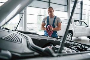 muss mal genauer hinschauen. Mann in blauer Uniform arbeitet mit kaputtem Auto. Reparaturen vornehmen foto