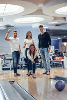 Komm schon, streik. Junge, fröhliche Freunde haben an ihren Wochenenden Spaß im Bowlingclub foto