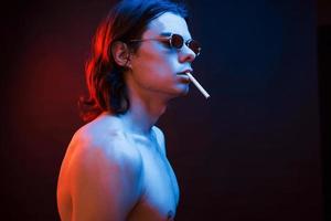 Zigarette rauchen. Studioaufnahme im dunklen Studio mit Neonlicht. Porträt eines ernsthaften Mannes foto