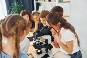 Mädchen, das Mikroskop untersucht. gruppe von kinderschülern im unterricht in der schule mit lehrer foto