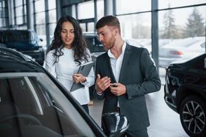 Ich bin sehr beeindruckt von diesem neuen Fahrzeug. Kundin und moderner stylischer bärtiger Geschäftsmann im Autosalon foto