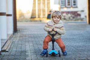 kleiner Kleinkindjunge reitet und sein Rollerfahrrad im Sommer