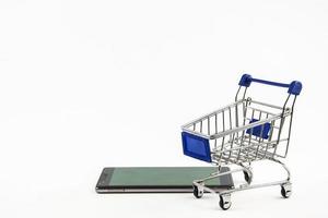 Smartphone mit Einkaufswagen auf weißem Hintergrund bedeutet Online-Shopping foto