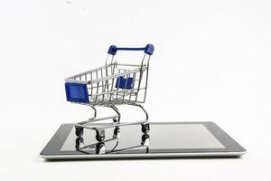 Einkaufswagen mit Tablet auf weißem Hintergrund, bedeutet Online-Shopping foto