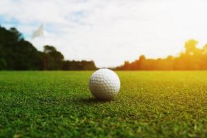 Golfball auf grünem Gras mit Loch und Sonnenlicht foto