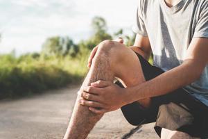 Männer, die sich beim Sport verletzt haben, halten Ihre Knie im Park mit den Händen foto