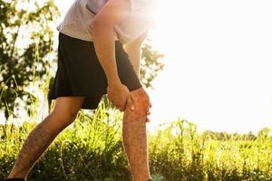 Männer, die sich beim Sport verletzt haben, halten Ihre Knie im Park mit den Händen foto