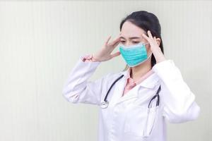 asiatische ärztin, die mit maske im untersuchungsraum sitzt und über gesundheitsversorgung, umweltverschmutzung pm2.5, neues normal- und coronavirus-schutzkonzept nachdenkt. foto