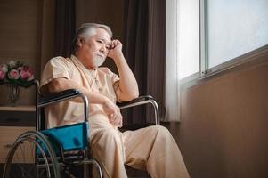 älterer männlicher Patient mit grauen Haaren, der im Rollstuhl sitzt und sich deprimiert und einsam fühlt, während er im Privatzimmer des Krankenhauses nachdenkt foto