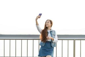 Aufgeregtes junges Mädchen, das ein Selfie macht, während es an der Brücke steht foto
