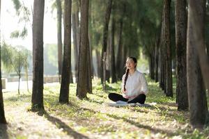 junge asiatische frau, die meditiert im grünen park, gesundes lebensstilkonzept. foto