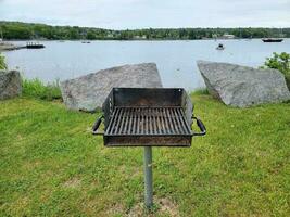 Grill im Gras in der Nähe des Sees mit Booten und Felsen foto