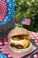 Vierter Juli Käseburger mit amerikanischer Flagge auf dem Picknicktisch im Freien foto