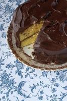 Schokoladenglasur auf gelbem Kuchen mit auf blauem Blumenhintergrund ausgeschnittener Scheibe foto