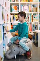 Ein kleiner Junge greift in der Buchhandlung nach einem Regal mit Kinderbüchern. foto