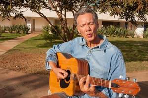 glücklicher reifer Mann, der im Park seine Akustikgitarre singt und spielt foto