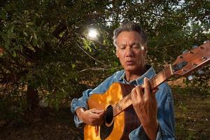 glücklicher reifer Mann, der im Park seine Akustikgitarre singt und spielt foto