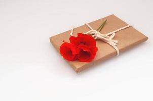 Als Geschenk in Bastelpapier eingewickelt liegt oben ein Strauß roter Mohnblumen foto