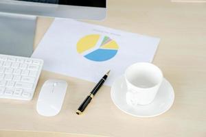 Geschäfts- und Arbeitsplatzkonzept. Tasse heißen Kaffee auf dem Schreibtisch mit Computertastatur und Papiergrafiken foto