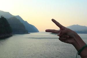 zwei-finger-symbol, zeigefinger und mittelfinger, symbol des friedens auf den hintergrundbergen, flüssen und blauer himmel attraktive natur foto