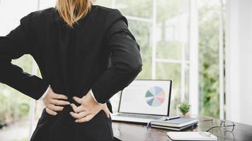 junge Geschäftsfrau im Büro mit schrecklichen Rückenschmerzen foto