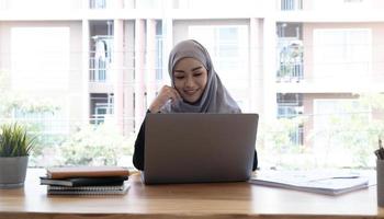 Junge asiatische muslimische Geschäftsfrau in eleganter Freizeitkleidung, die über Geschäfte spricht und lächelt, während sie im kreativen Coworking sitzt. foto