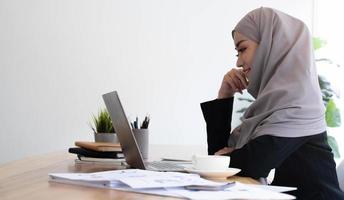 Junge asiatische muslimische Geschäftsfrau in eleganter Freizeitkleidung, die über Geschäfte spricht und lächelt, während sie im kreativen Coworking sitzt. foto