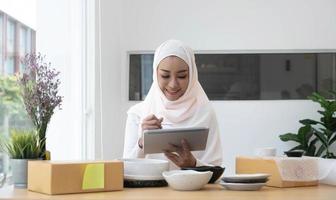 attraktive muslimische unternehmerin, e-commerce-geschäftsinhaberin, die eine versandbox in ihrem büro vorbereitet. foto