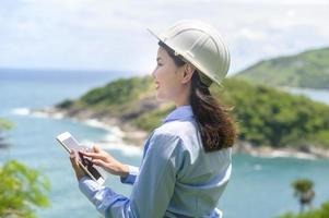 Ingenieurin, die am Meer arbeitet und einen Schutzhelm trägt foto