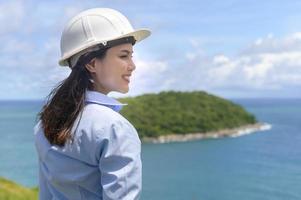 Ingenieurin, die am Meer arbeitet und einen Schutzhelm trägt foto