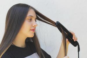 Porträt eines jungen Mädchens, das einen Haarglätter für lockiges Haar verwendet und ihr Haar mit einem Bügeleisen bügelt foto