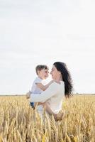 glückliche familie von mutter und kleinkind, die auf weizenfeld gehen, familienporträt foto