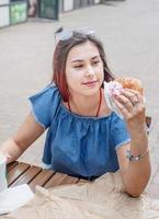 stilvolle tausendjährige frau, die im sommer burger im straßencafé isst foto