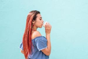 Fröhliche, trendige Frau mit roten Haaren, die Kaffee trinkt und auf blauem Wandhintergrund auf der Straße tanzt foto