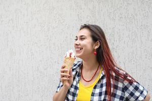 Fröhliche, trendige Frau mit roten Haaren, die auf der Straße Eis isst foto