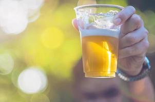 Celebration Beer Cheers Concept - Nahaufnahme der Hand, die während seines Siegeswettbewerbs oder seiner erfolgreichen Aufgabenbesprechung Biergläser des jungen Mannes auf einer Party im Freien hochhält foto