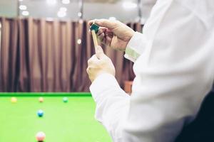 snooker-spieler, der wartet, halten seinen queue-stick und kreide bereiten sich während des wettbewerbsspiels auf seine drehung vor foto