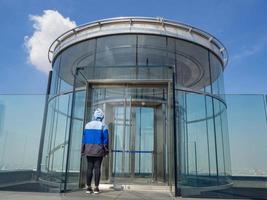 Rückansicht einer Frau, die mit dem Glas des Tunnels mit Aufzug steht foto