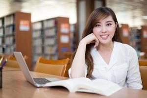 schöne asiatische Studentin mit Laptop für das Studium in der Bibliothek foto