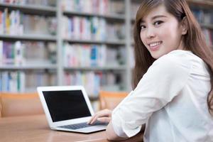 schöne asiatische Studentin mit Laptop für das Studium in der Bibliothek foto