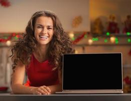 Hausfrau zeigt Laptop leeren Bildschirm in der Weihnachtsküche foto
